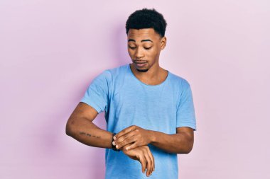 Rahat ve kendinden emin genç Afro-Amerikalı bir adam, günlük mavi tişört giyip saati kontrol ediyor. 