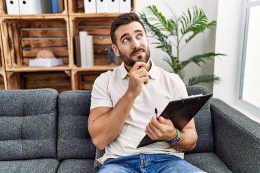 Psikoloji kliniğinde çalışan yakışıklı İspanyol bir adam. Elleri çenesinde soru sorarken, düşünceli bir ifade takınıyor. Gülümseyen ve düşünceli bir yüz. şüphe kavramı. 