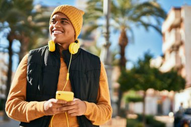 Genç Latin adam şehirde kulaklık takarak mutlu gülümsüyor.