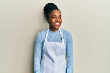 Saçları örgülü, daha temiz önlüklü ve eldivenli, yüzünde gülümseme, doğal bir ifade olan Afro-Amerikan kadın. Kendinden emin gülen. 
