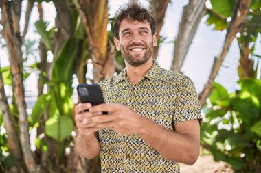 Parkta akıllı telefon kullanarak gülümseyen İspanyol genç adam.