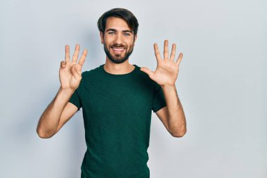 Gündelik beyaz tişört giyen genç İspanyol adam 8 numarayı gösterip işaret ederken kendinden emin ve mutlu gülümsüyor.. 