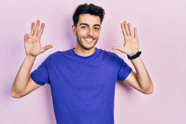 Gündelik tişört giyen İspanyol genç adam dokuz numarayı gösterip işaret ederken kendinden emin ve mutlu bir şekilde gülümsüyor.. 