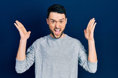 Gündelik kıyafetler giyen genç İspanyol adam başarı için deli ve çılgınlığı kutluyor kollarını kaldırmış ve gözlerini kapatmış heyecanla bağırıyor. Kazanan konsept 