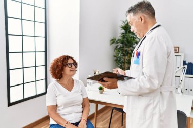 Doktor üniforması giyen orta yaşlı bir adam ve kadın klinikte tıbbi danışmanlık yapıyorlar.