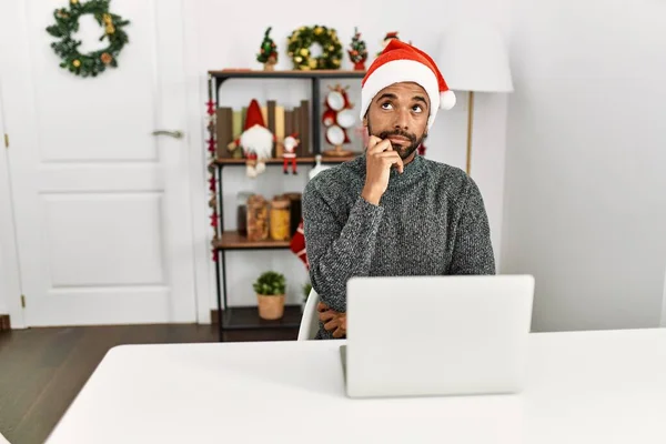 带着胡子 头戴圣诞帽的年轻人 用笔记本电脑认真地思考着手托着下巴的问题 思考着令人困惑的想法 — 图库照片