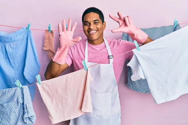 Jovem Homem Hispânico Bonito Vestindo Avental Mais Limpo Segurando Roupas — Fotografia de Stock