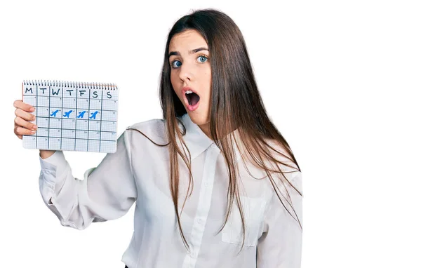 Young Brunette Teenager Holding Travel Calendar Scared Amazed Open Mouth — Stock Photo, Image