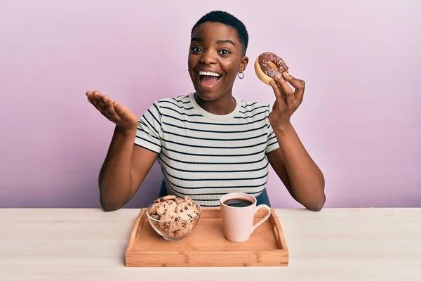 Młoda Afroamerykanka Jedząca Śniadanie Trzymając Pączka Czekoladowego Świętując Osiągnięcie Szczęśliwym — Zdjęcie stockowe