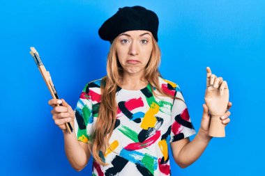 Kafkasyalı genç bir kadın sanatçı elinde küçük ahşap bir manikin ve boya fırçaları tutuyor. Depresyonda ve endişe içinde, kızgın ve korkmuş bir halde. hüzünlü ifade. 