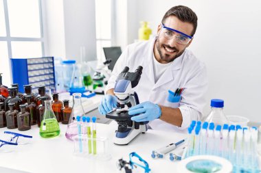 Laboratuvarda mikroskop kullanarak bilim adamı üniforması giyen genç bir İspanyol.