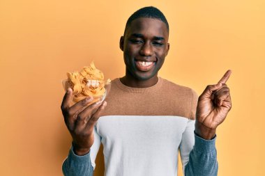 Genç Afro-Amerikan adam elinde kaseyle pişmemiş spagetti ile gülümsüyor. 