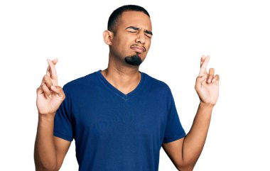 Sıradan tişörtler giyen Afro-Amerikalı genç adam umut ve gözler kapalı bir şekilde gülümseyerek parmaklarını çapraz yaptı. Şans ve batıl inançlar. 