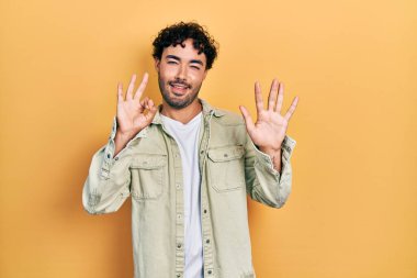 Gündelik kıyafetler giyen genç İspanyol adam sekiz numarayı gösterip işaret ederken kendinden emin ve mutlu bir şekilde gülümsüyor.. 