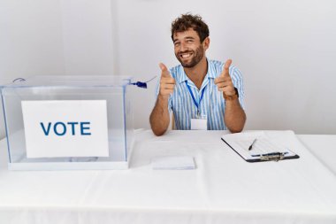 Siyasi seçimlerde genç ve yakışıklı bir adam oy pusulasında oturmuş mutlu ve komik yüzüyle kamerayı işaret ediyor. iyi enerji ve titreşimler. 