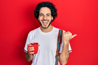 Yakışıklı İspanyol bir adam kahve içiyor başparmağını kaldırıyor ve ağzı açık gülümsüyor. 