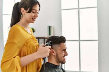Genç İspanyol kuaför kadın güzellik merkezinde tıraş makinesi kullanarak adamın saçını kesiyor..