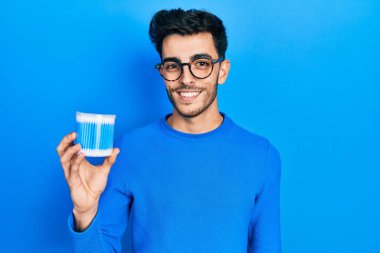 Kulak kiri temizleyici tutan genç İspanyol adam pozitif ve mutlu görünüyor ve kendine güvenen bir gülümsemeyle dişlerini gösteriyor. 