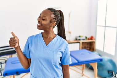 Saçları örgülü zenci bir kadın ağrı kesici kliniğinde çalışıyor. Gururlu görünüyor, gülümsüyor. Kenarda baş parmak hareketi yapıyor. 