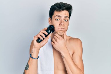 Elektrikli tıraş makinesiyle tıraş olan genç İspanyol adam komik suratlı yanakları şişiriyor. Ağzı havayla şişer, havayı yakalar.. 