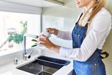 Genç sarışın kadın mutfakta kendinden emin bir şekilde gülümsüyor.