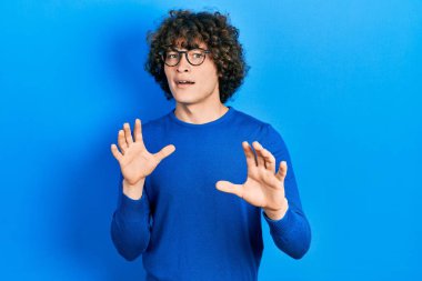 Sıradan kıyafetler ve gözlük takan yakışıklı genç adam korku ifadesinden korkuyor ve dehşete düşüyor. El hareketlerini bırak, şok içinde bağır. panik konsepti. 