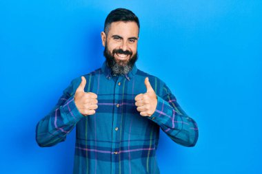 Gündelik kıyafetler giyen genç İspanyol adam. Başarı işareti yapıyor. Elleriyle olumlu jest yapıyor. Neşeli ifade ve kazanan jest. 