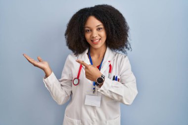 Genç Afro-Amerikan kadın doktor üniforması ve steteskop giyiyor kameraya hayret ediyor ve gülümsüyor.. 