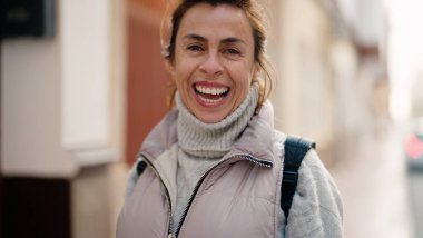 Orta yaşlı İspanyol kadın sokakta kendine güvenerek gülümsüyor.