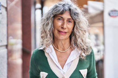 Orta yaşlı bir kadın sokakta kendine güvenerek gülümsüyor.