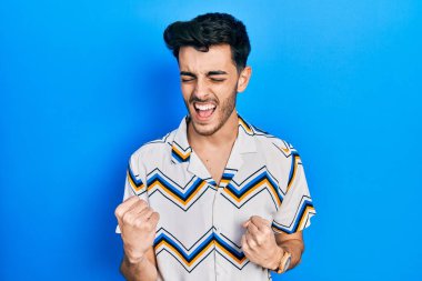 Gündelik giysiler giyen genç İspanyol adam kolları havada ve gözleri kapalı bir şekilde başarının şaşkınlığını ve şaşkınlığını yaşıyor. Kazanan konsept. 