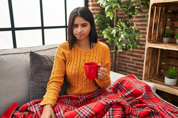 Kanepede oturan Latin asıllı genç kadın evde şüpheci ve gergin bir şekilde kahve içiyor, sorun yüzünden surat asıyor. negatif kişi. 