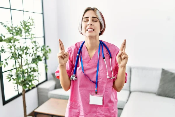 Young Beautiful Woman Wearing Doctor Uniform Stethoscope Gesturing Finger Crossed — Stock Photo, Image