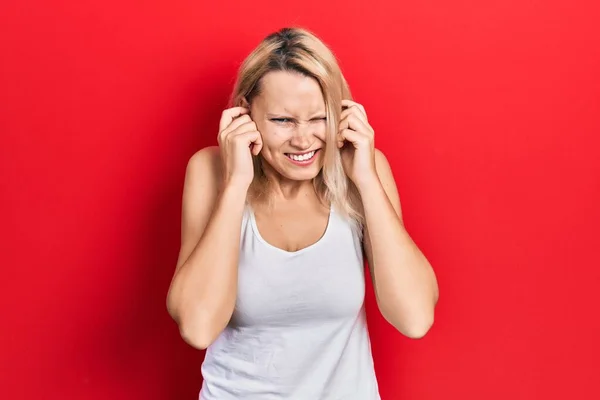 美丽的高加索金发女人穿着宽松的白色T恤 用手指捂住耳朵 带着恼怒的表情 听着嘈杂的音乐 聋人概念 — 图库照片