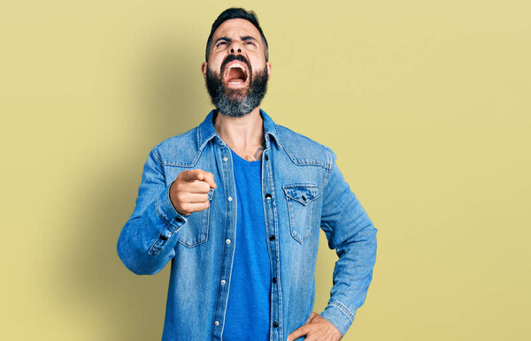 Латиноамериканец с бородой, указывающий пальцем в камеру злой и безумный кричащий расстроенный и разъяренный, кричащий от гнева, глядя вверх. 