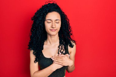 Kıvırcık saçlı, sıradan giyinen, kolsuz tişörtlü, göğsünde elleri kapalı, yüzünde minnet ifadesi olan İspanyol bir kadın. sağlık kavramı. 