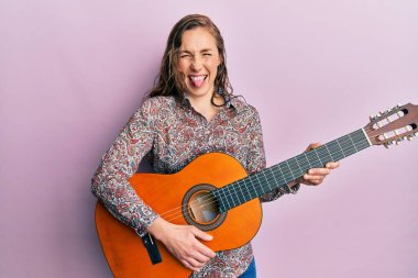 Klasik gitar çalan genç sarışın kadın komik bir ifadeyle dilini dışarı çıkarıyor.. 