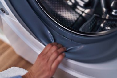 Çamaşır odasında çamaşır makinesi açan genç bir kadın.