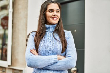 Şehirde kollarını kavuşturup gülümseyen İspanyol genç kız.