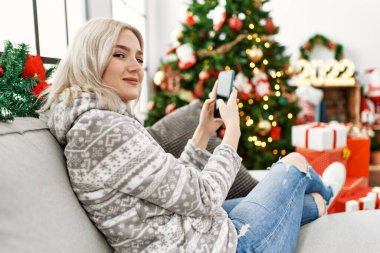 Evdeki akıllı telefonu kullanarak kanepede oturan beyaz bir kız..