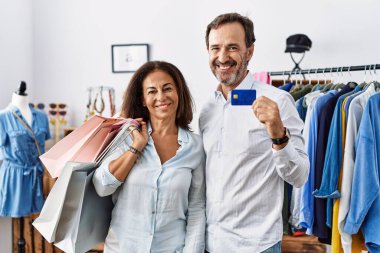 İspanyol orta yaşlı çift ellerinde alışveriş torbaları ve mutlu ve havalı bir gülümsemeyle kredi kartı tutuyorlar. şanslı kişi. 