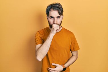 Sakallı, sıradan sarı tişörtlü beyaz bir adam kendini iyi hissetmiyor ve soğuk algınlığı veya bronşitin belirtisi olarak öksürüyor. sağlık hizmeti kavramı. 