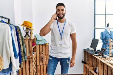 Genç Arap esnaf akıllı telefondan konuşuyor giyim mağazasında elbise rafının yanında duruyor.