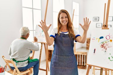 Resim stüdyosunda önlük giyen İspanyol kadın 10 numarayı gösterip işaret ederken kendine güvenen ve mutlu bir şekilde gülümsüyor.. 