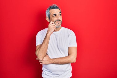 Gri saçlı, beyaz tişört giyen, yakışıklı, orta yaşlı bir adam ciddi bir yüz ifadesi olan, eli çenesinde soru soran, kafa karıştırıcı bir fikir olan. 