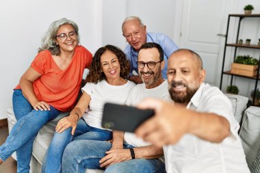Gülümseyen bir grup orta yaşlı arkadaş evdeki akıllı telefonun yanında selfie çekiyorlar..