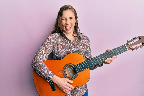 Joven Mujer Rubia Tocando Guitarra Clásica Sacando Lengua Feliz Con — Foto de Stock