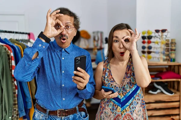 소매점에서 스마트폰을 사용하는 중년의 이인종 커플들이 얼굴로 손가락을 바라본 충격을 — 스톡 사진
