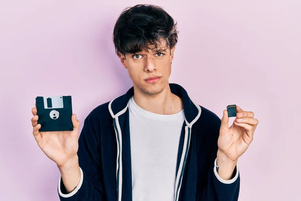 Przystojny Hipsterski Młody Człowiek Trzymający Dyskietkę Kartę Sdxc Sceptyczny Nerwowy — Zdjęcie stockowe