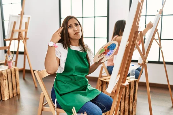 若いヒスパニック系のアーティストの女性は アートスタジオで絵を描き 銃のように頭に手や指を指して自分自身を殺し 自殺のジェスチャー — ストック写真